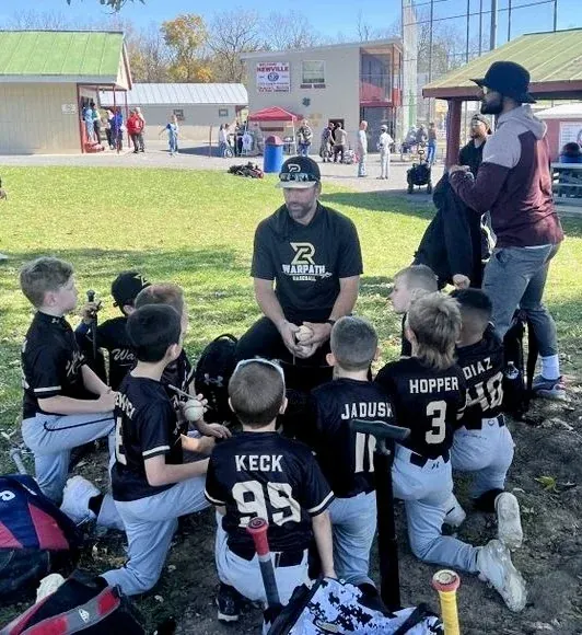 A coach talking to a huddle of young Warpath players