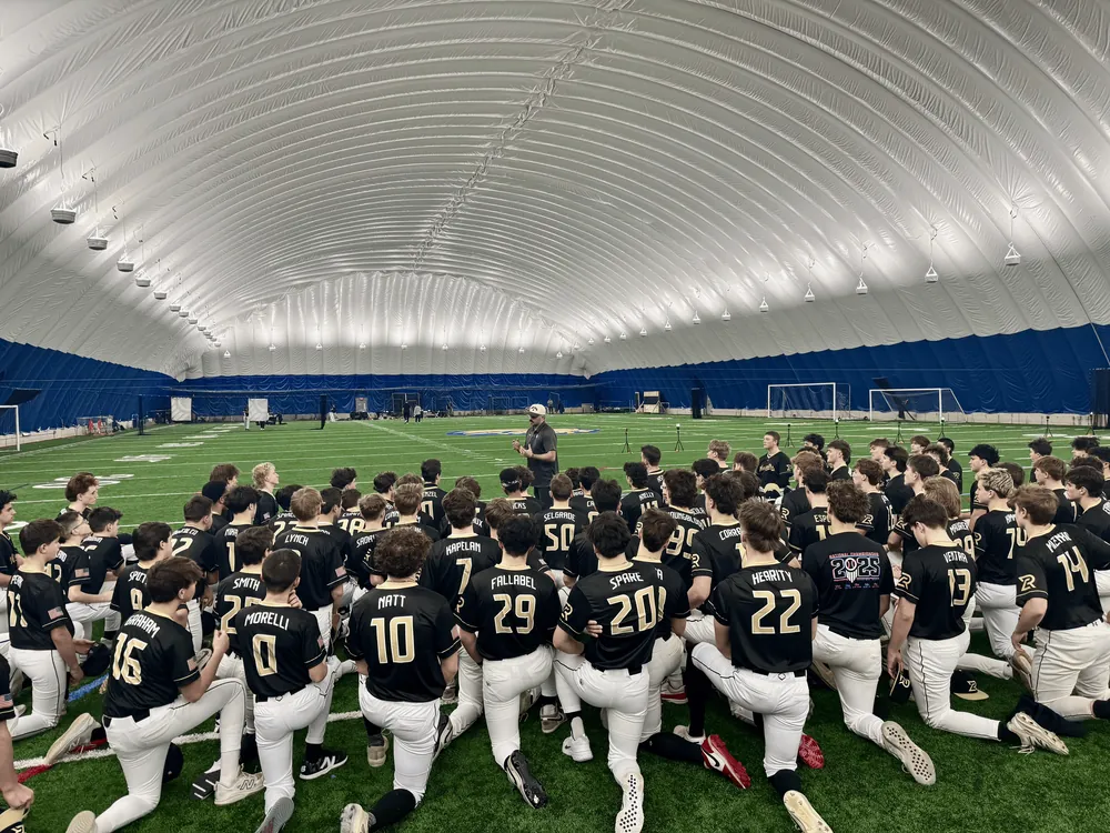 Warpath players in black and gold jerseys kneeling around a coach inside an indoor dome